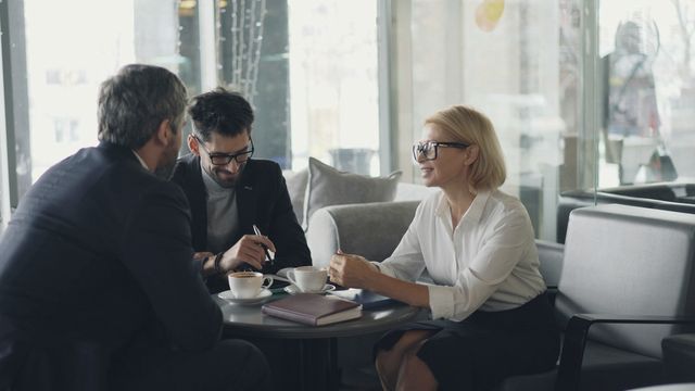 Una sessione di lavoro a un tavolo rotondo, con appunti e caffè tra tre persone