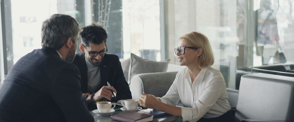 Una sessione di lavoro a un tavolo rotondo, con appunti e caffè tra tre persone