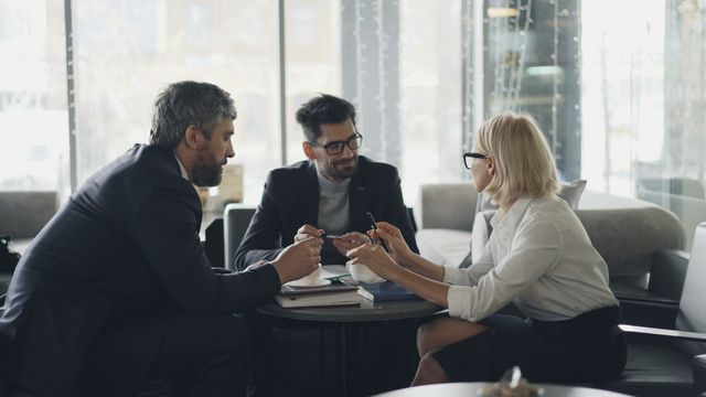 Tre persone in conversazione attorno a un tavolino, accanto a una grande vetrata