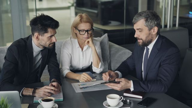 Tre persone che esaminano insieme documenti stampati e un grafico